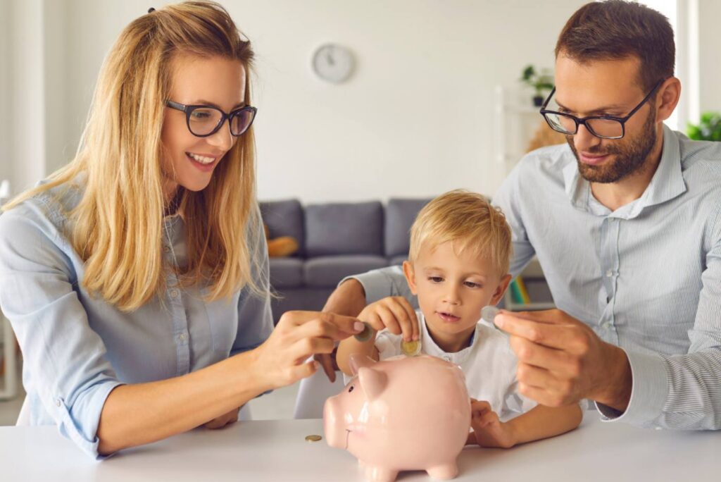 Mother and father with their son putting coins in pink piggybank
